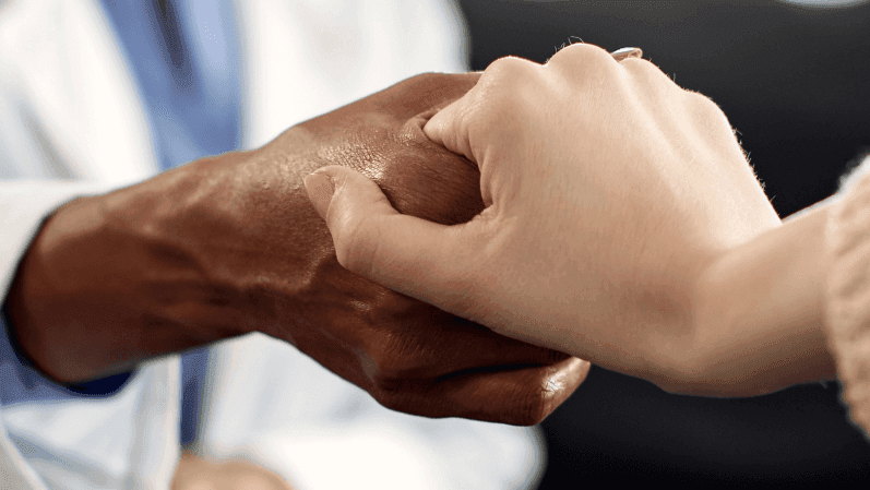 Close up of a therapist holding her patient's hand during a session, representing the importance of cancer research funding.